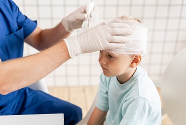 Das Bild zeigt ein Kind, das in der Klinik wegen einer Kopfverletzung verbunden wird (verweist auf: Kopfverletzungen bei Kindern: Hilfe auch für Familie gefragt)